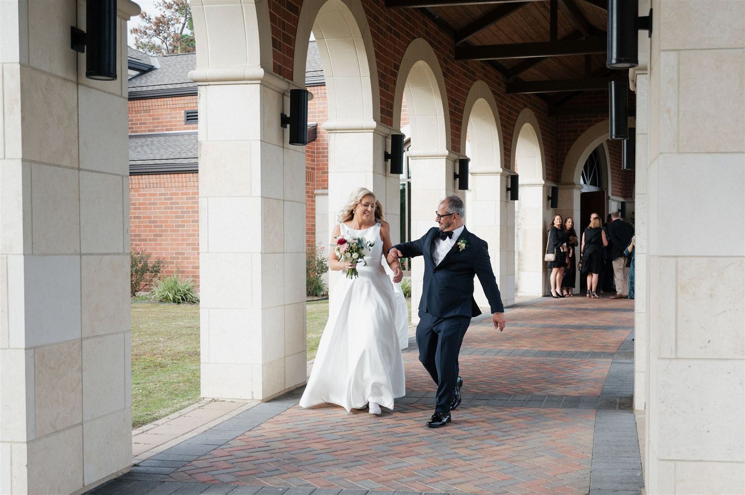 Couple walking through covered brick colonnade on wedding day.