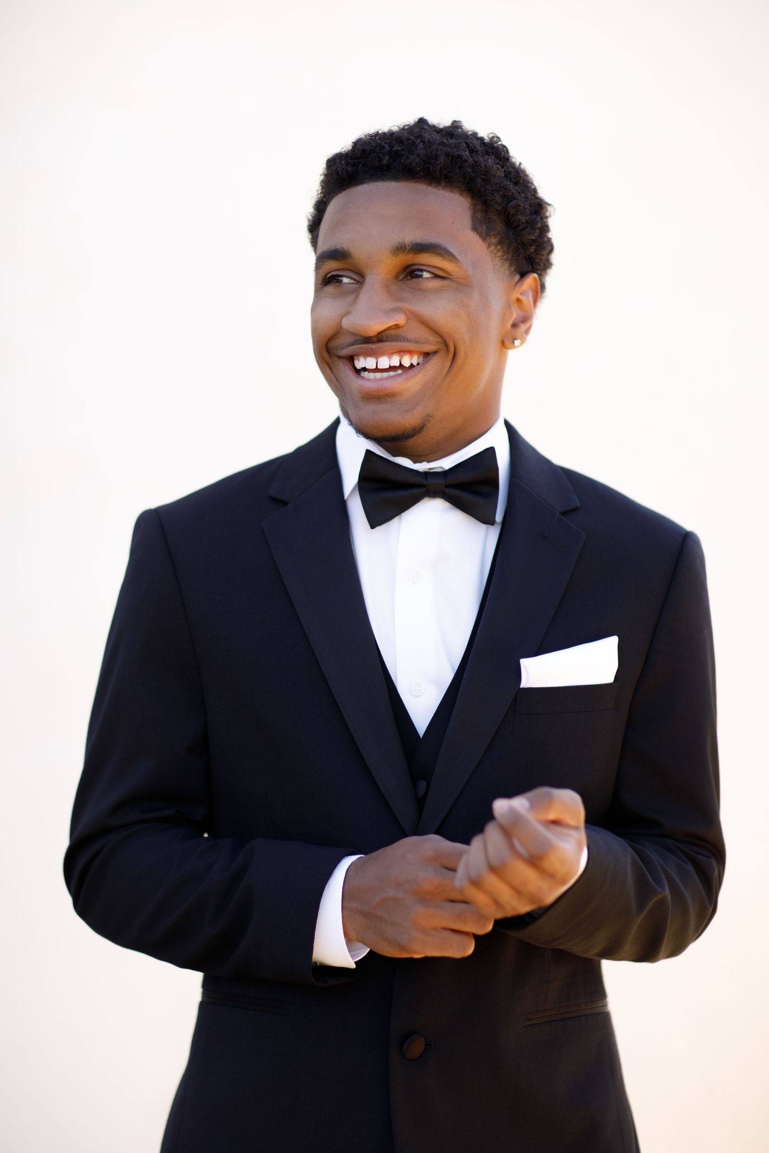 A high school senior in classic black tuxedo and bow tie smiling against light background.