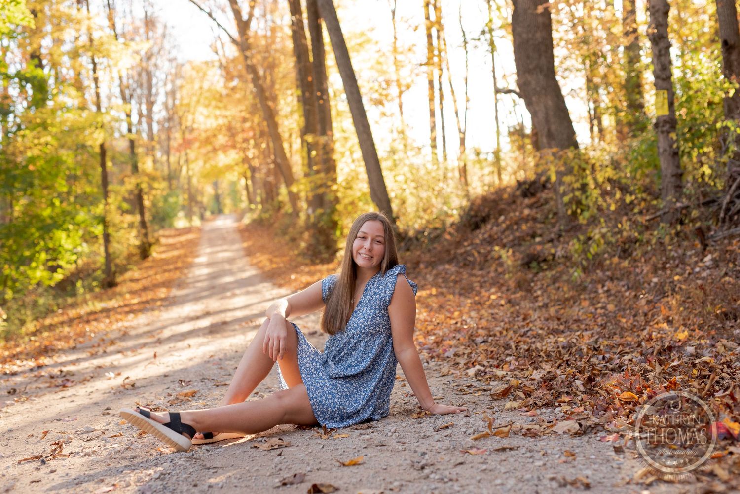 Casual outdoor portrait on a leaf-covered forest path during golden hour.