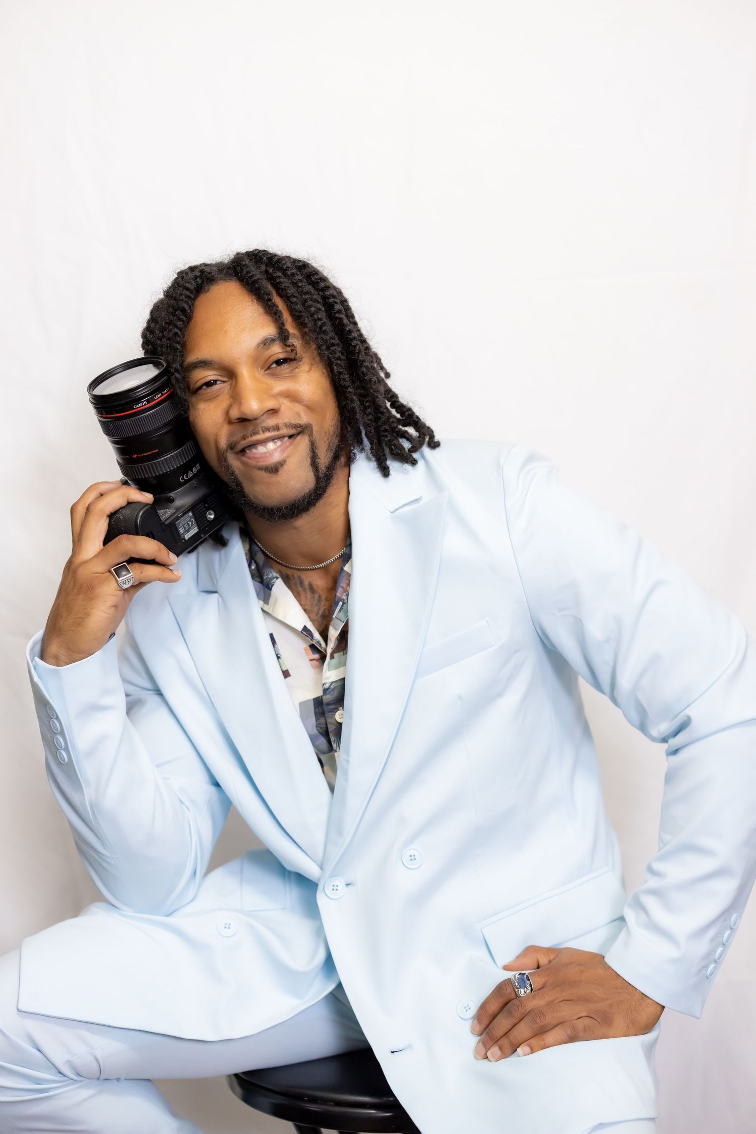 Professional photographer in light blue suit holding camera against white backdrop.