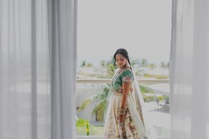 A traditional bride poses elegantly against white curtains with a scenic outdoor backdrop.
