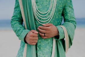 Detail shot of mint green sherwani with pearl necklaces and intricate embroidery.