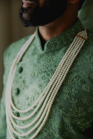 Close-up of mint green embroidered sherwani with pearl necklace detail.