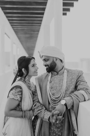 Black and white portrait of a couple in ornate wedding attire in a modern corridor.