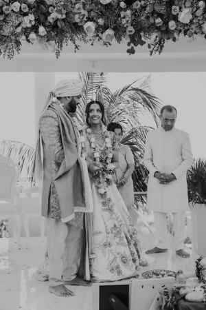 Black and white photograph of a traditional wedding ceremony under floral decorations.