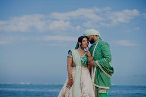 A couple in traditional wedding attire share an intimate moment by the ocean.