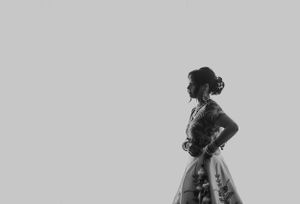 Artistic black and white profile shot of a bride in traditional lehenga with hands on hips.