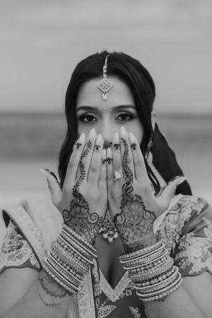 Black and white photo showing decorated hands with henna and bangles covering face.