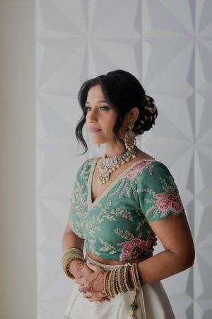 Woman in embroidered green and white lehenga with elegant jewelry and updo hairstyle.