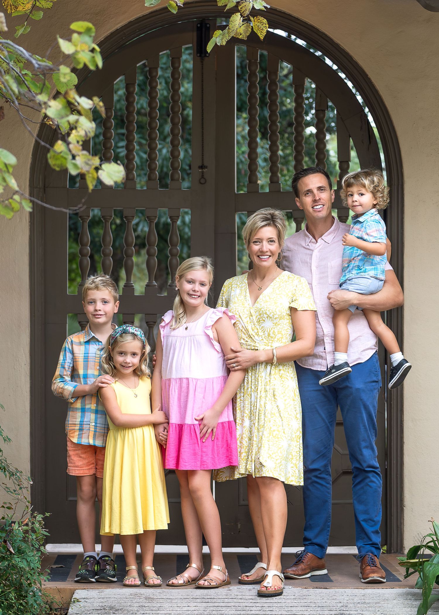 Family photo of mom and dad with four children smiling while standing infant of decorative door at Landa Library