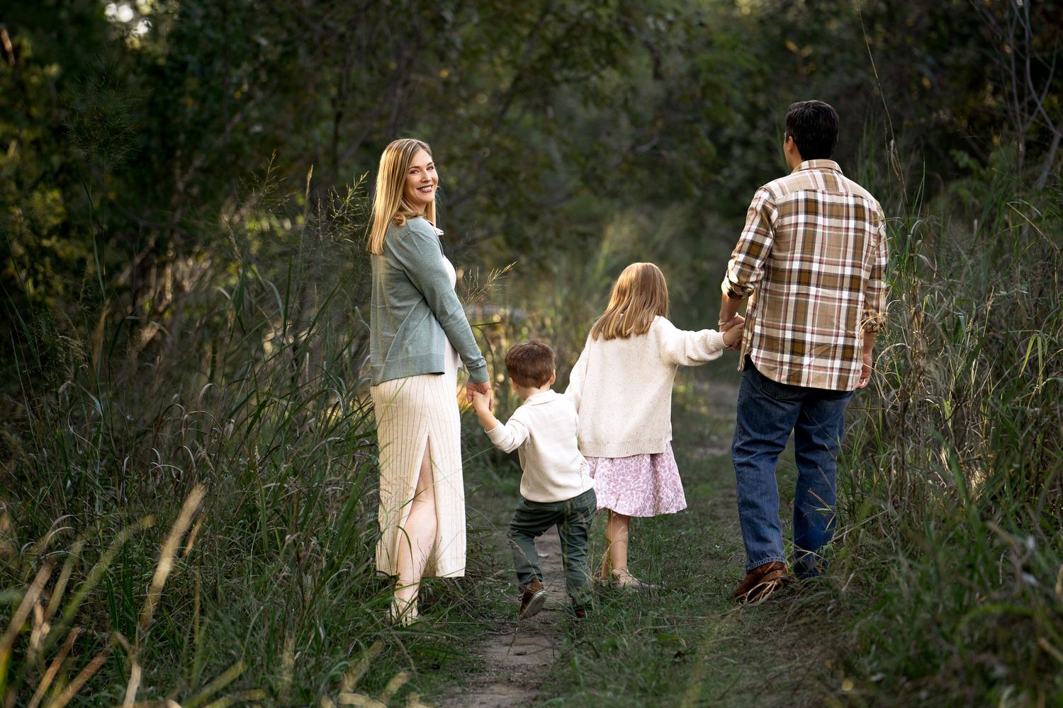 family portrait of mom, young son, school age girl and dad holding hands walking down a pathway at Cibolo Nature Center