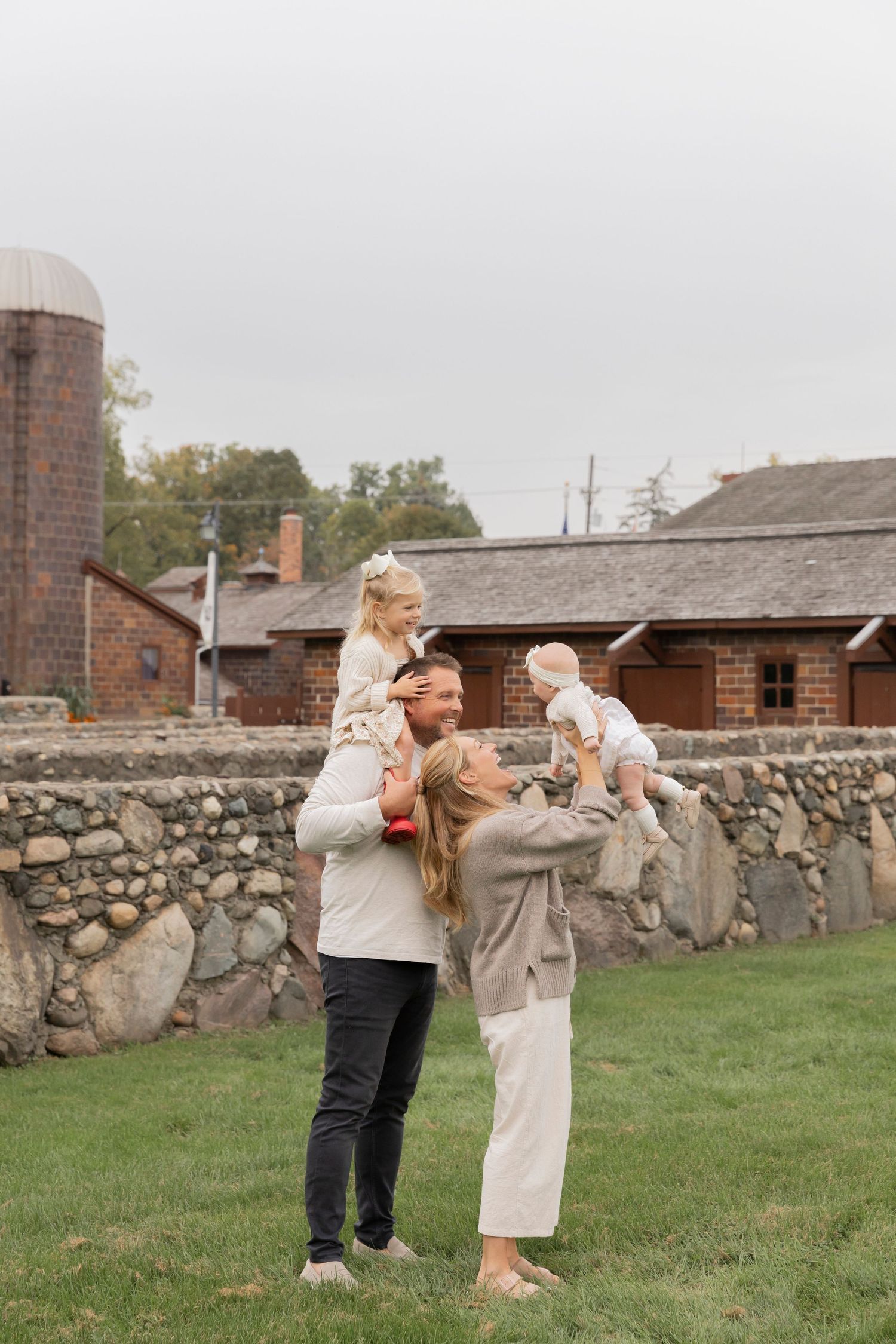 family of four wearing beige clothes playing in front of a historic farm in Rochester Hills michigan