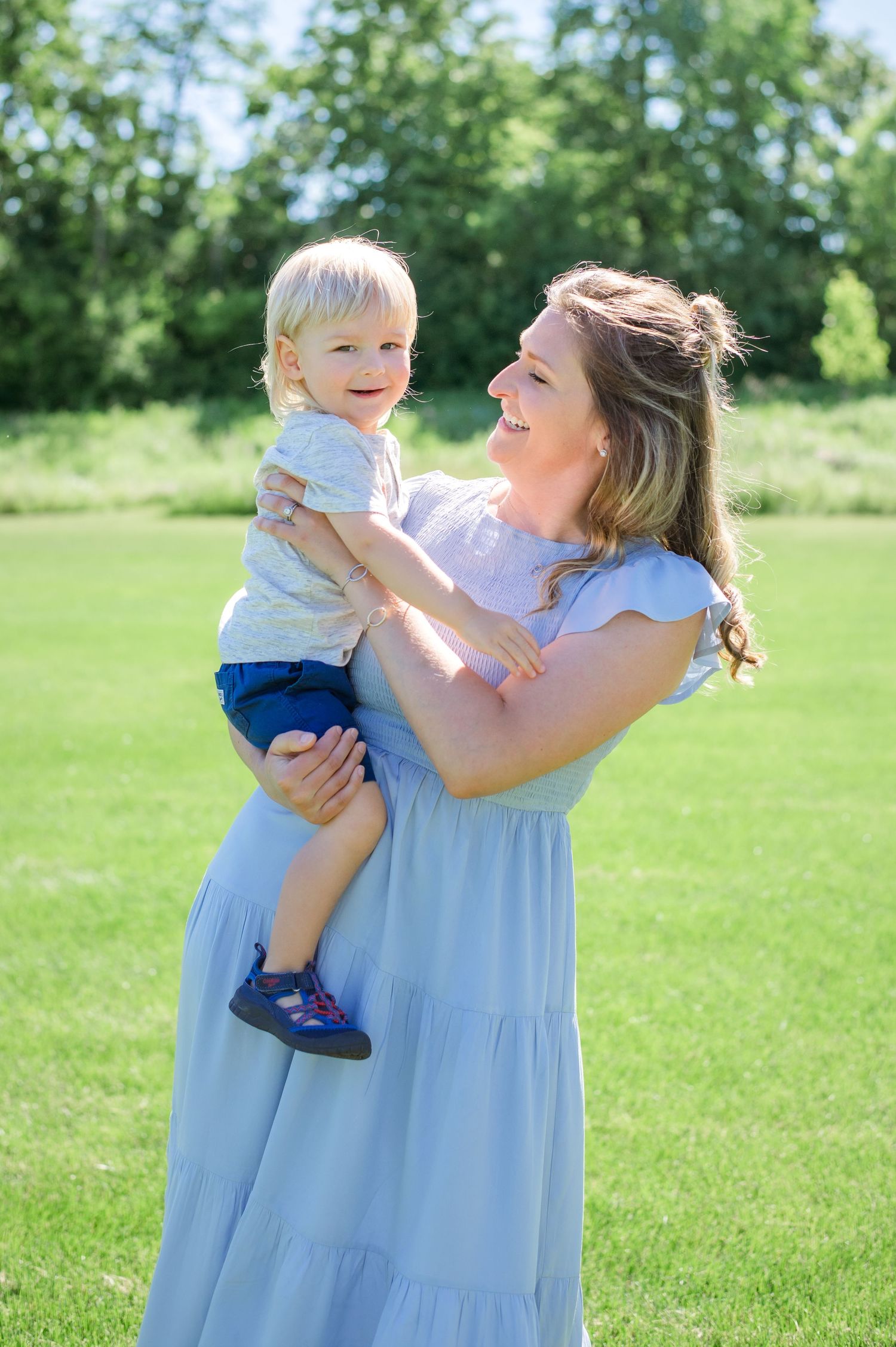 A parent holds a toddler while sharing joyful laughter in a sunlit meadow.