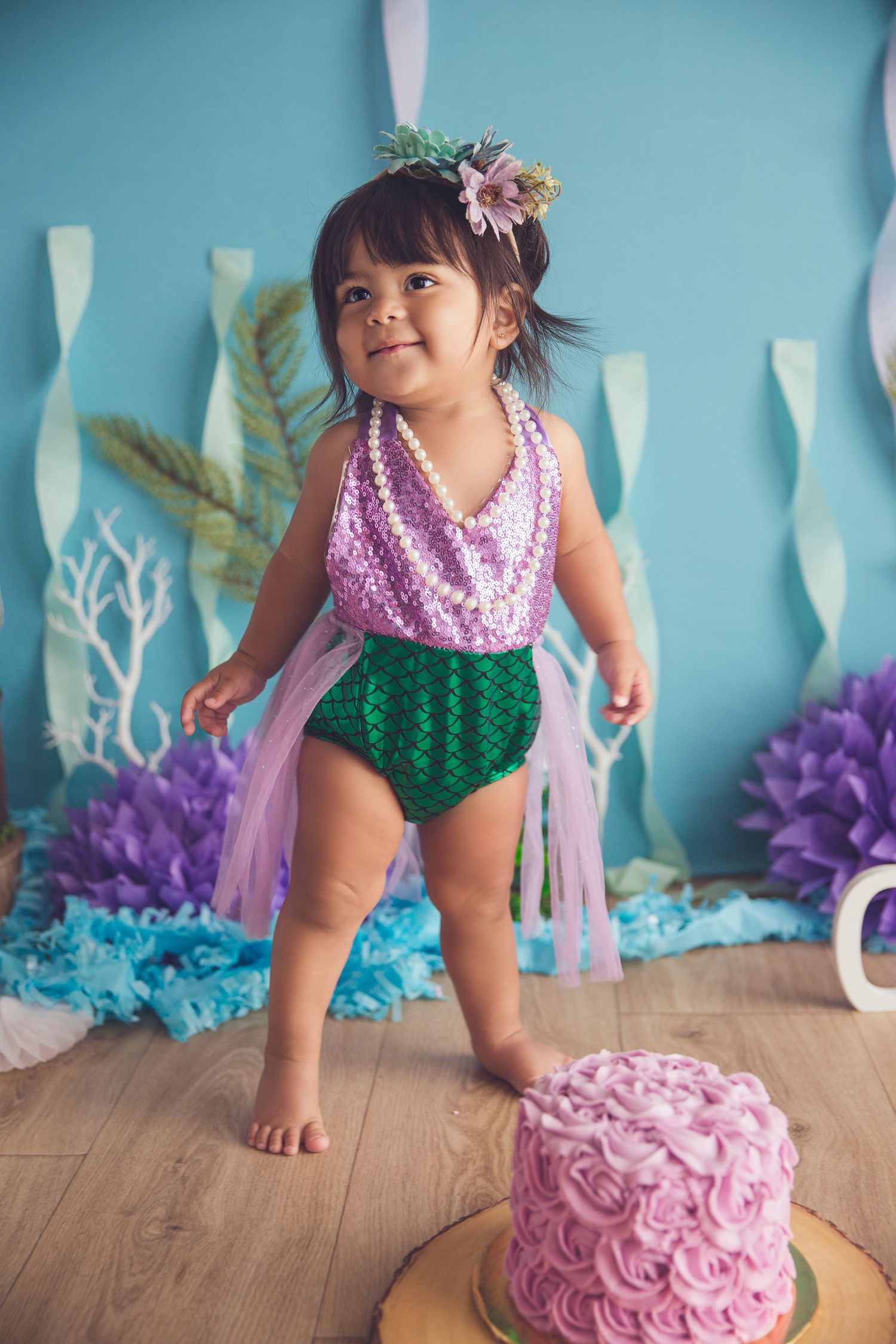 baby girl standing up in mermaid clothing and cake