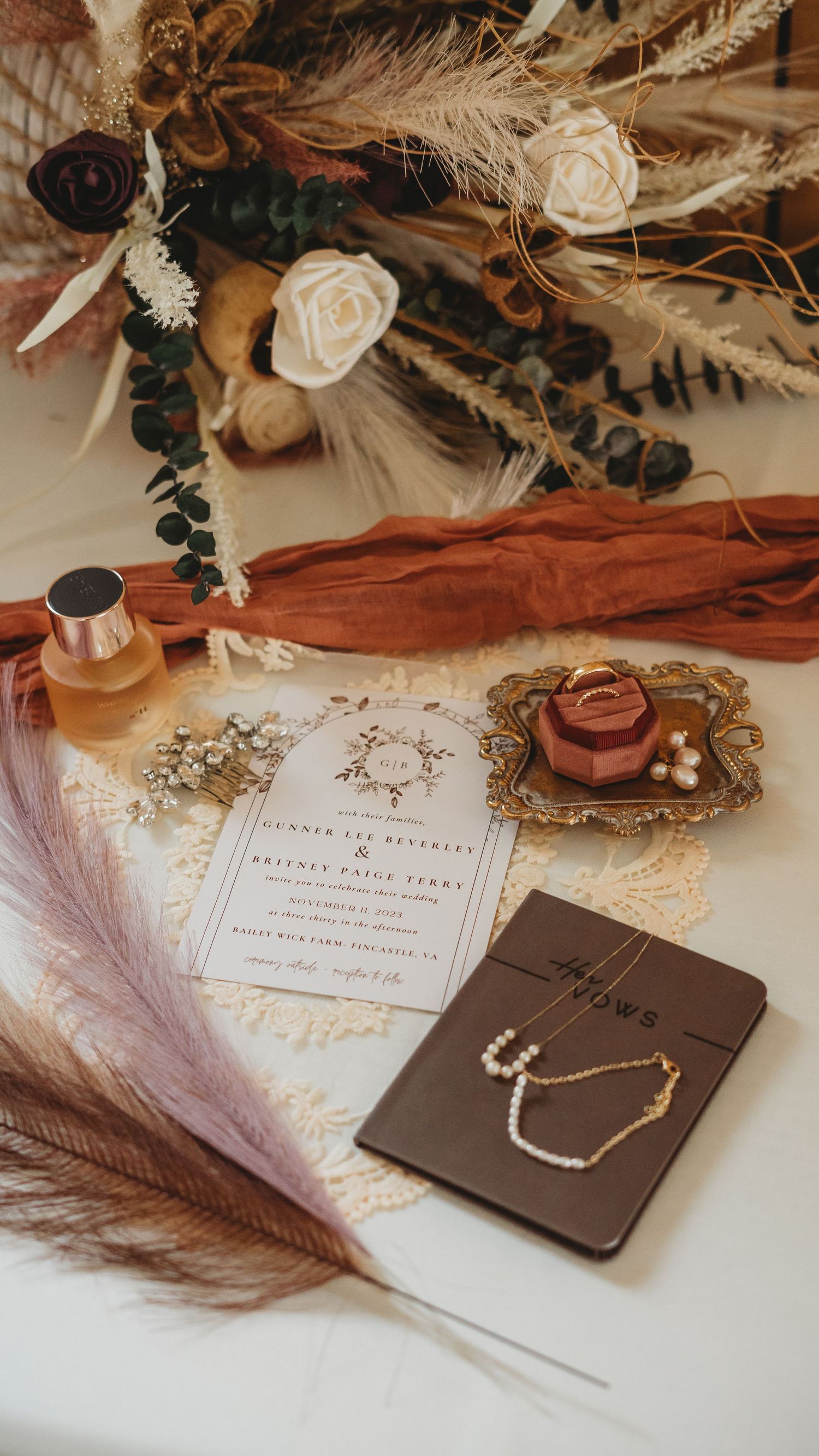 Wedding details flatlay with feathers, invitations and jewelry on textured background.