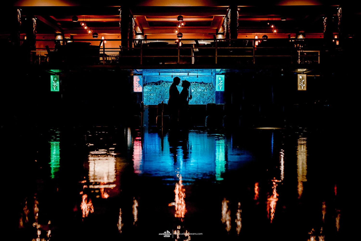 Silhouettes reflected in water with colorful lights creating a dramatic nighttime scene.
