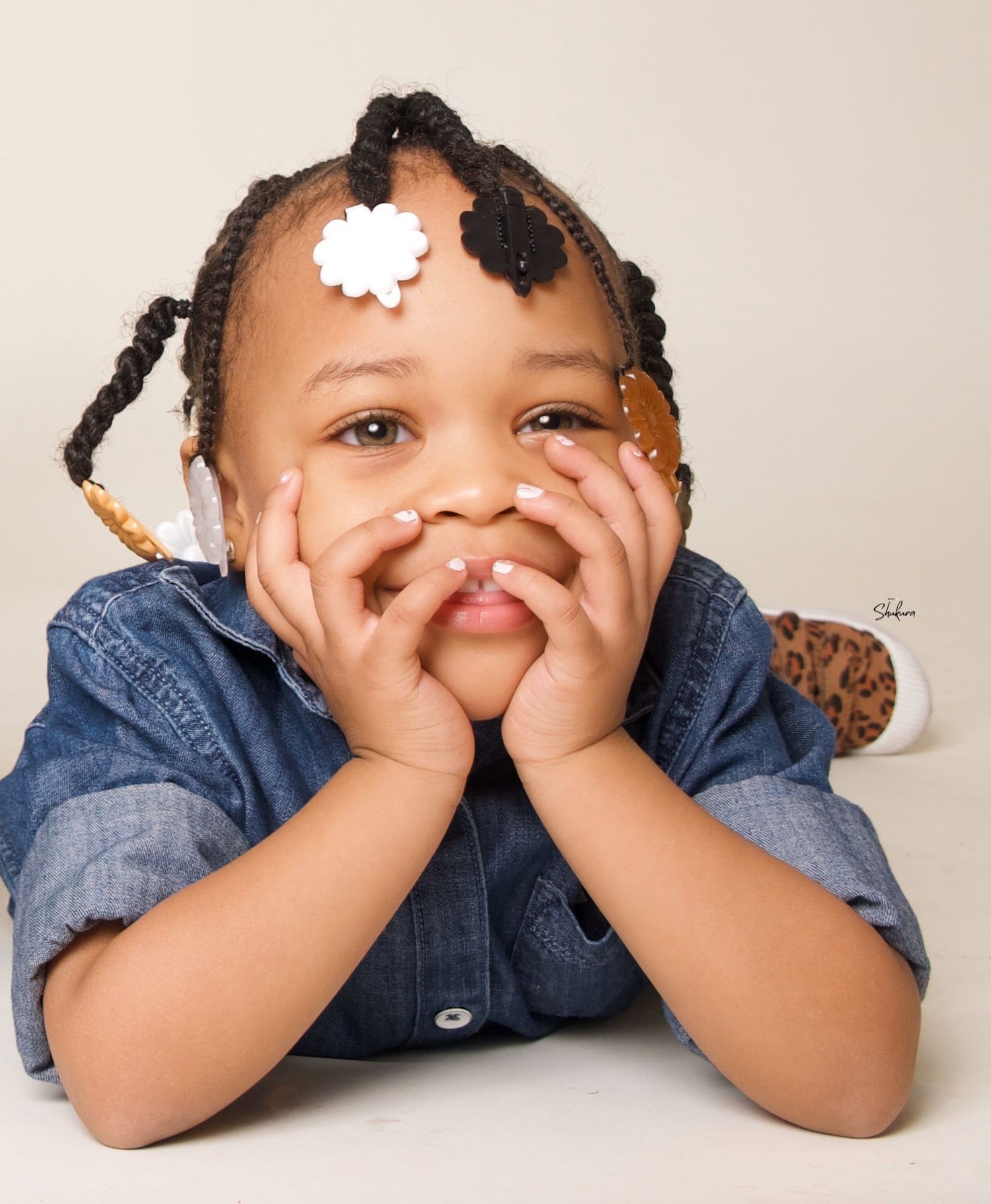 Child in denim shirt with braided hair and white hair clip poses playfully.