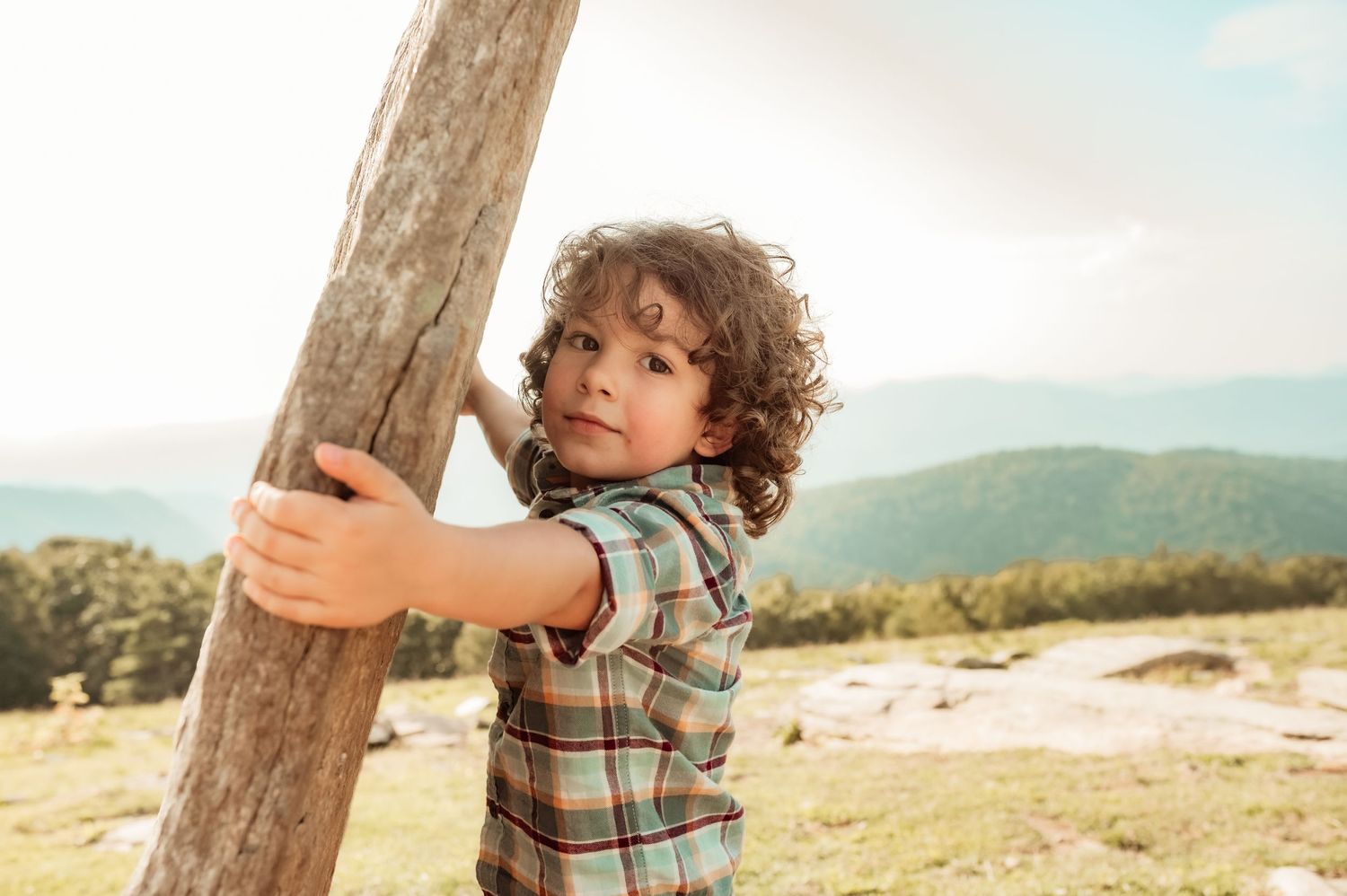 A boy hugs a rock with mountains behind him during family photoshoot.