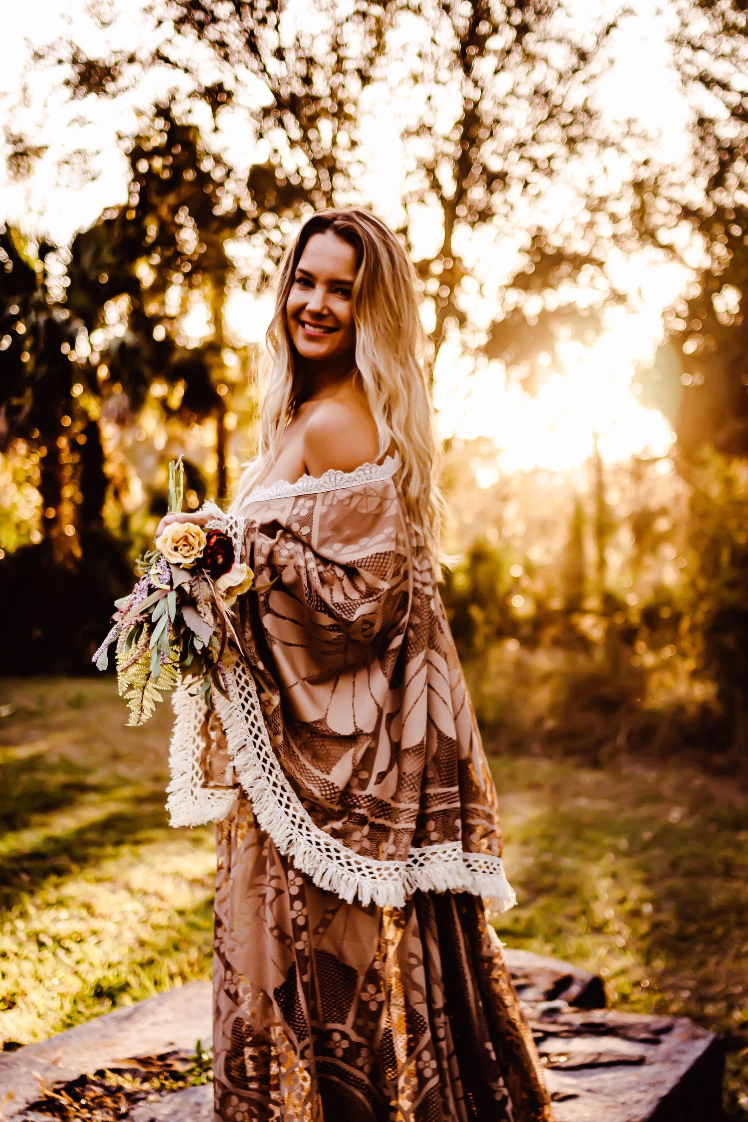 Woman in flowing vintage-style dress poses in golden sunlit forest.