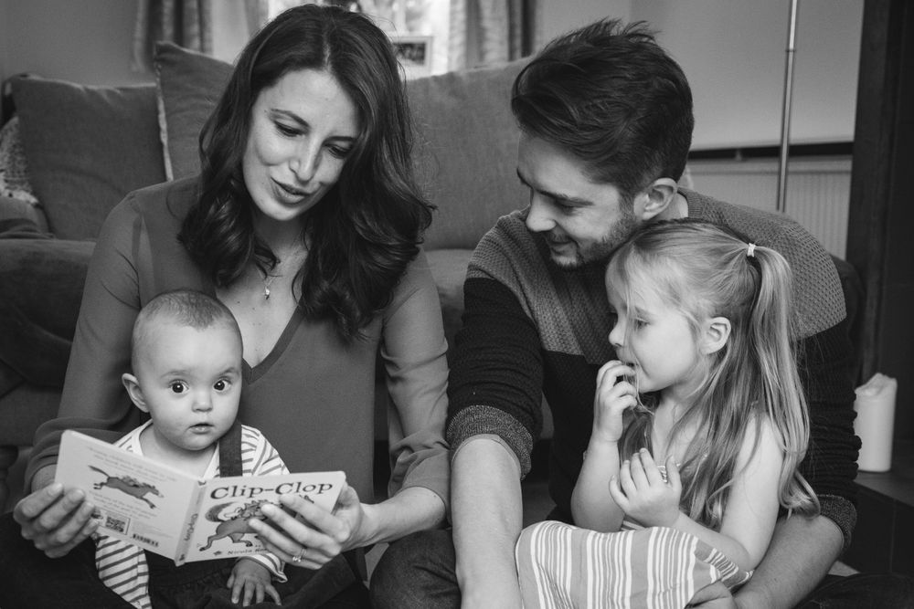 A family reads a storybook together on their living room couch.