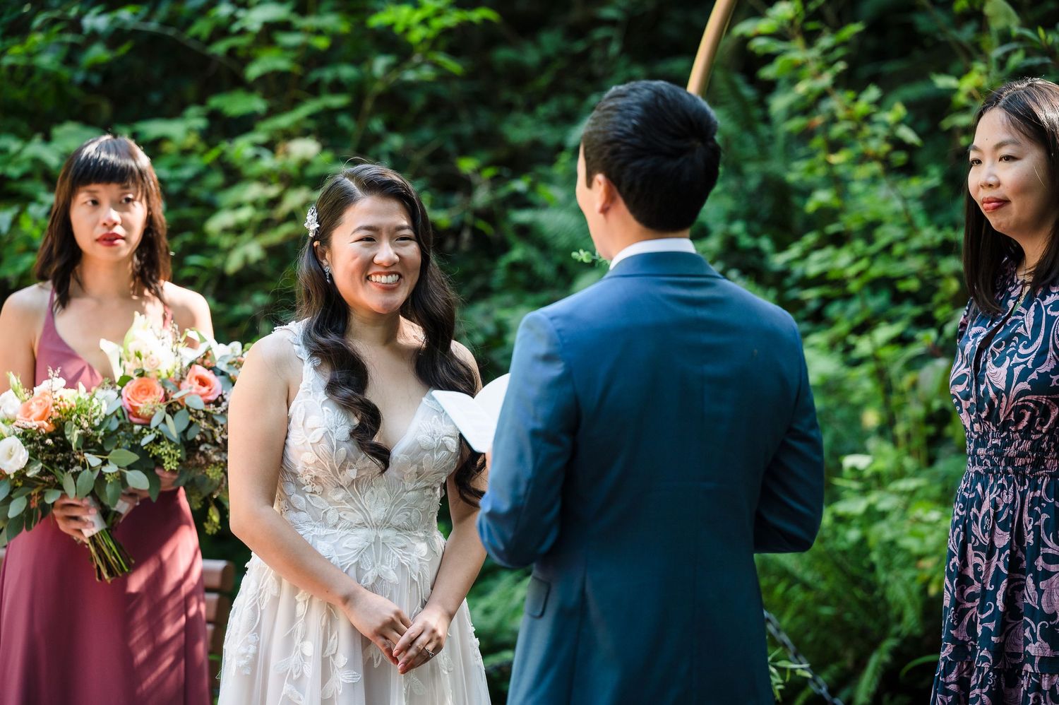 A wedding ceremony in progress with attendants in burgundy dresses under forest canopy.