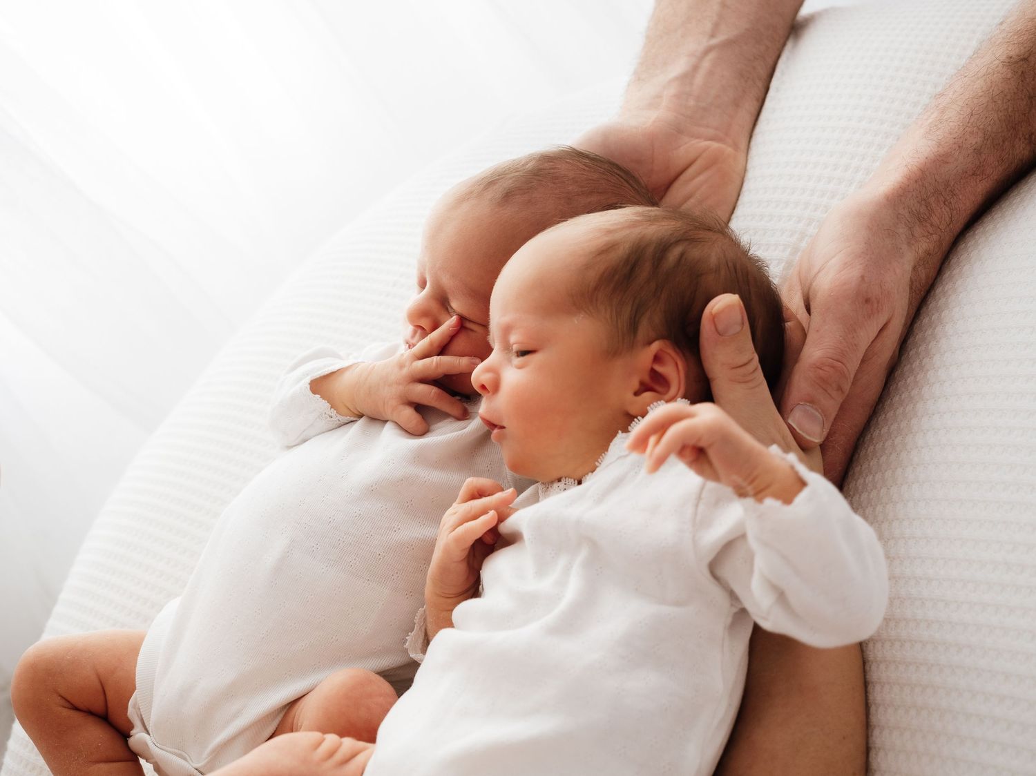 Newborn baby twins laying together on a white blanket with parents hands under them, Didcot baby photoshoot by Verity