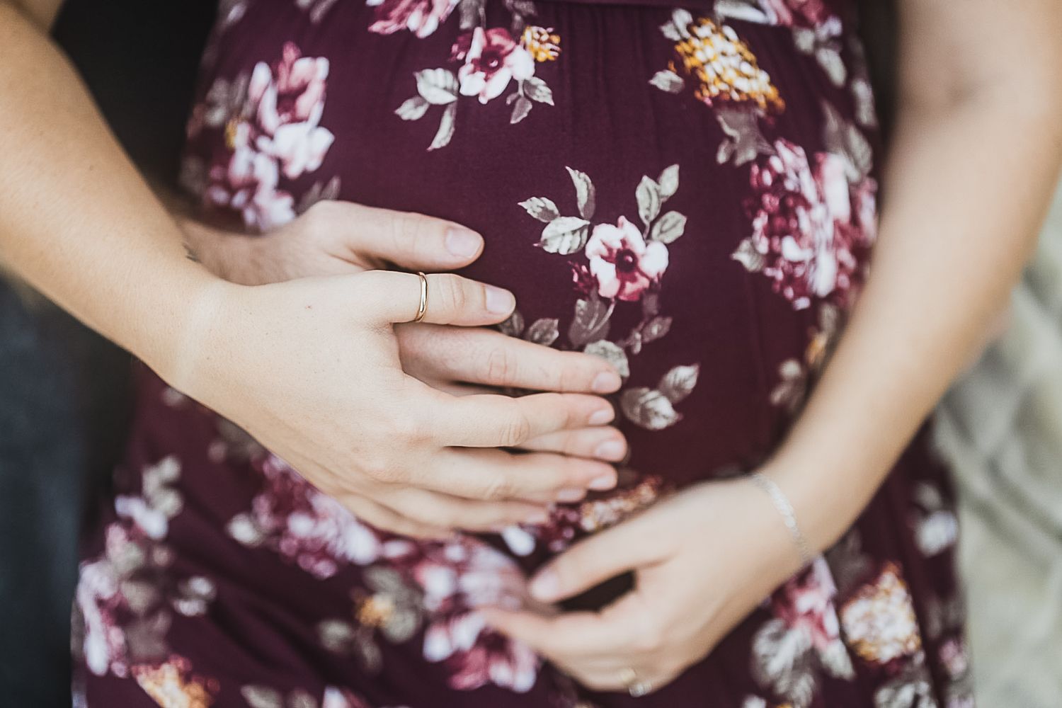 Close-up of hands cradling a pregnant belly in a floral burgundy maternity dress.