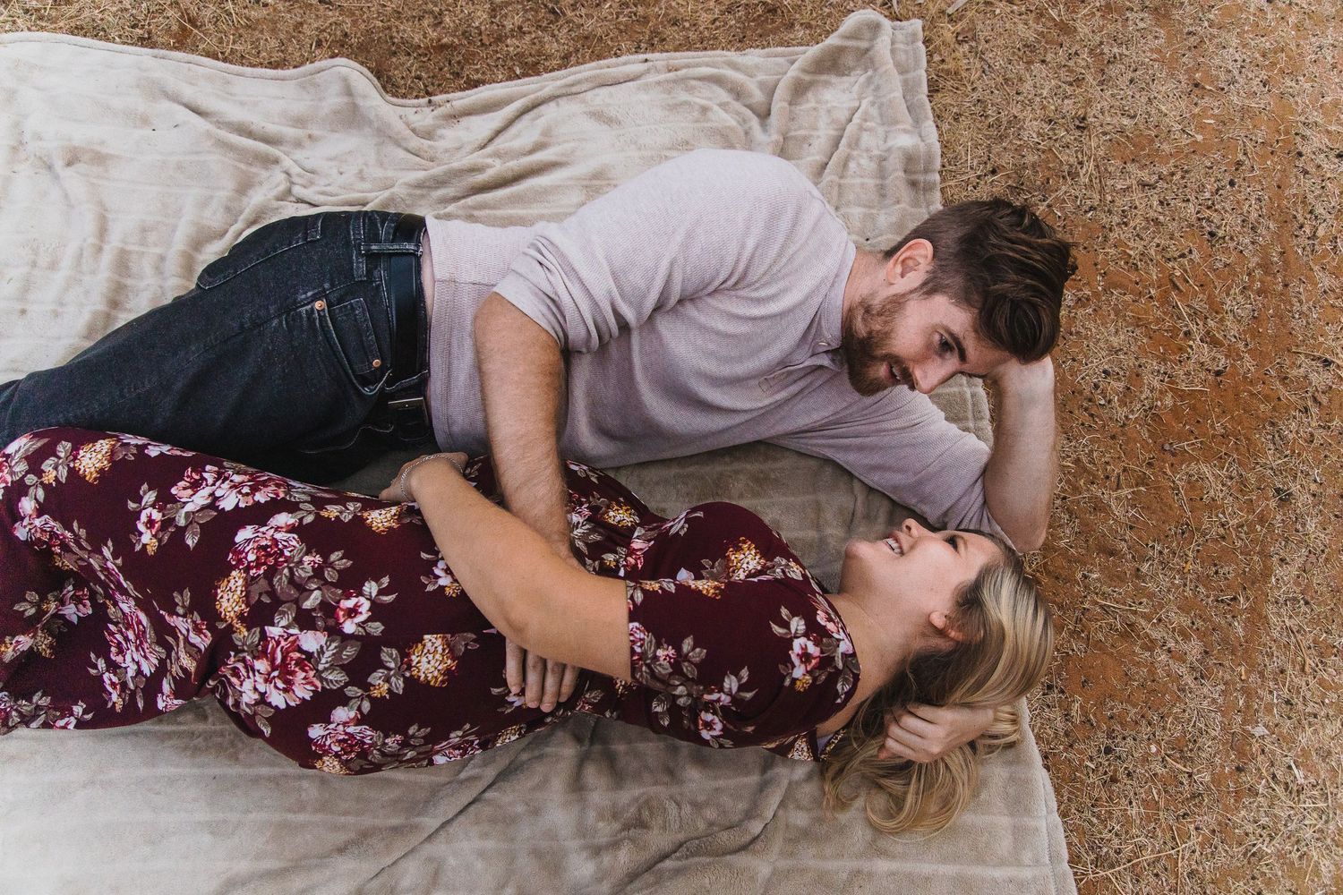 A tender moment between two people lying on a white blanket outdoors.