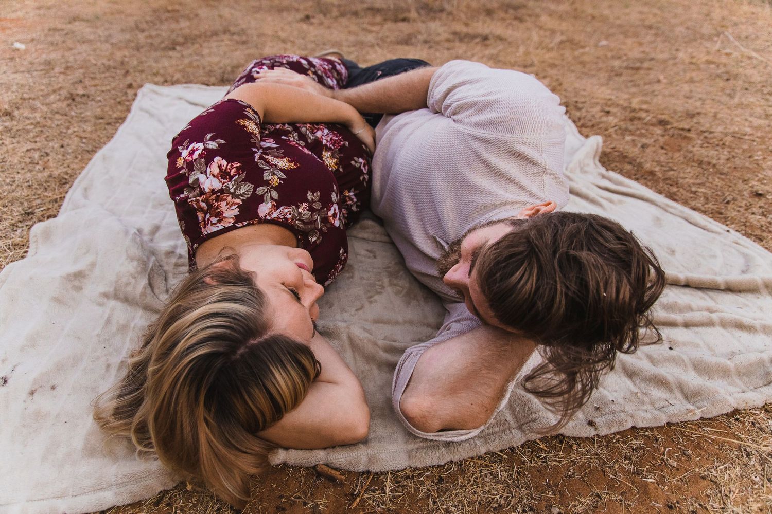 A couple lies together on a blanket in a field during a photo session.
