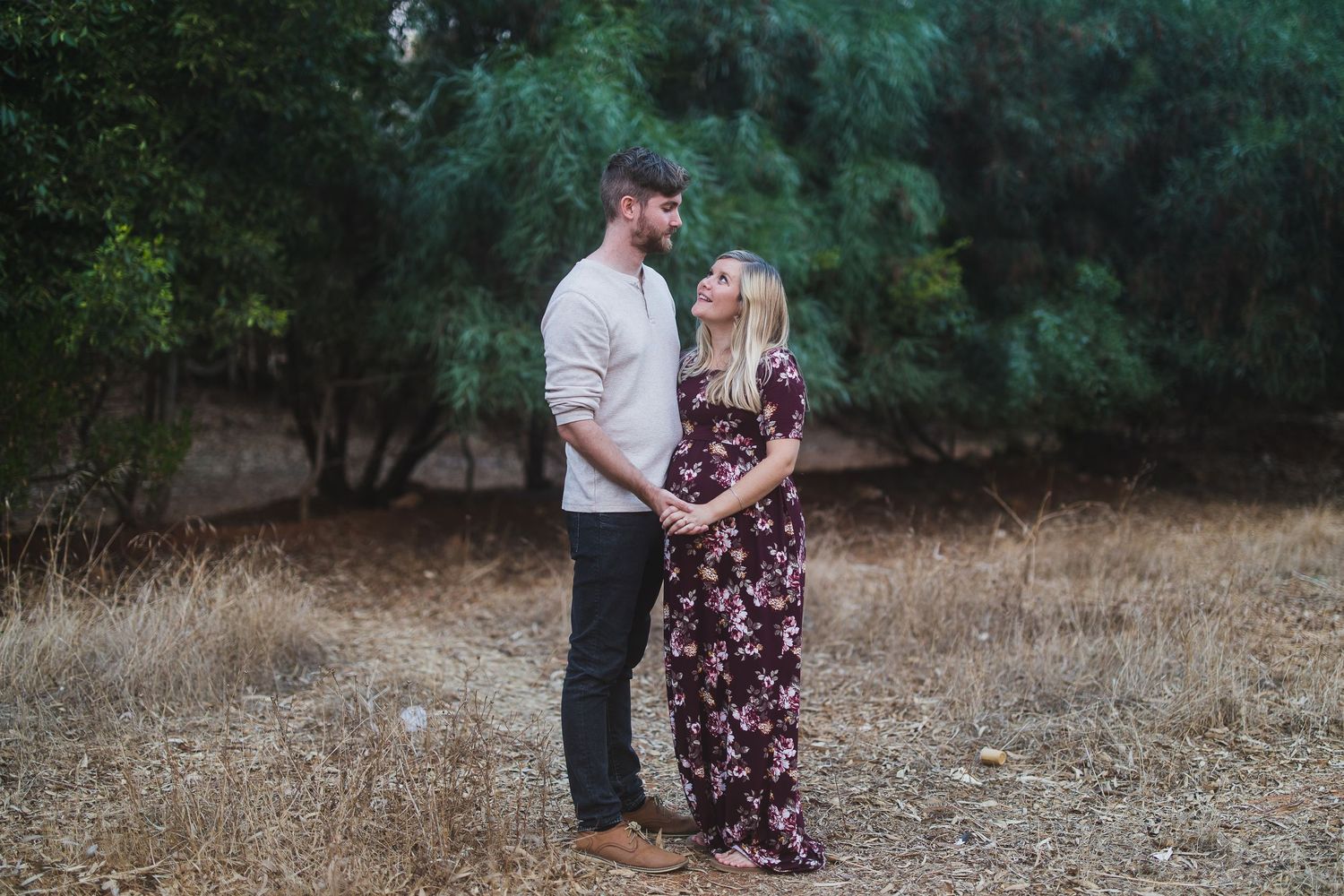 A tender outdoor portrait of a couple standing together in a natural setting with trees.