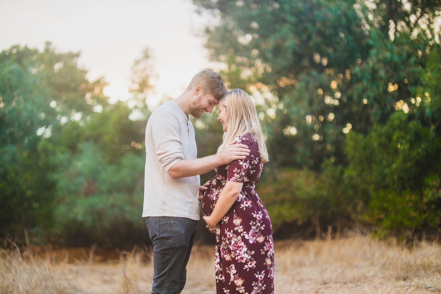Sunset photoshoot of couple in casual attire against wooded backdrop.