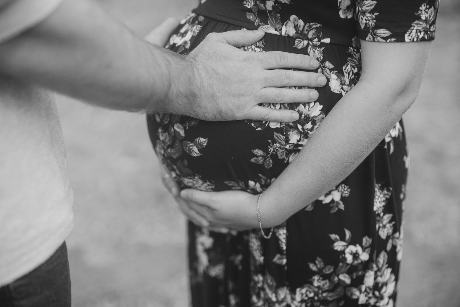Black and white detail shot of hands tenderly placed on a pregnant belly in a floral dress.