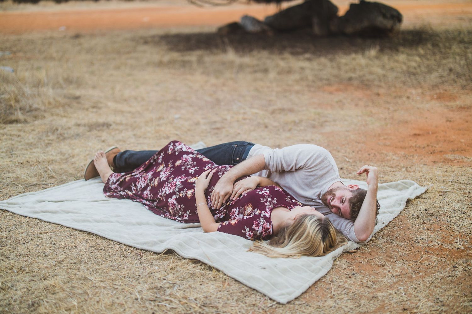 A couple relaxing on a white blanket in an outdoor setting with reddish soil.