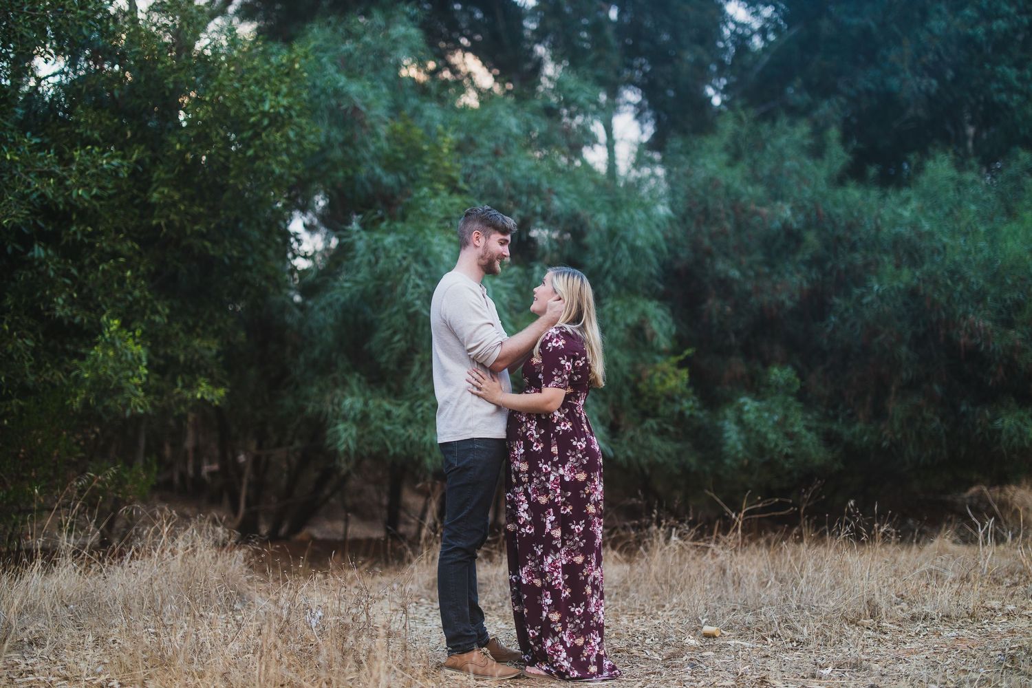 Romantic outdoor photoshoot of a couple against a backdrop of trees and dry grass.