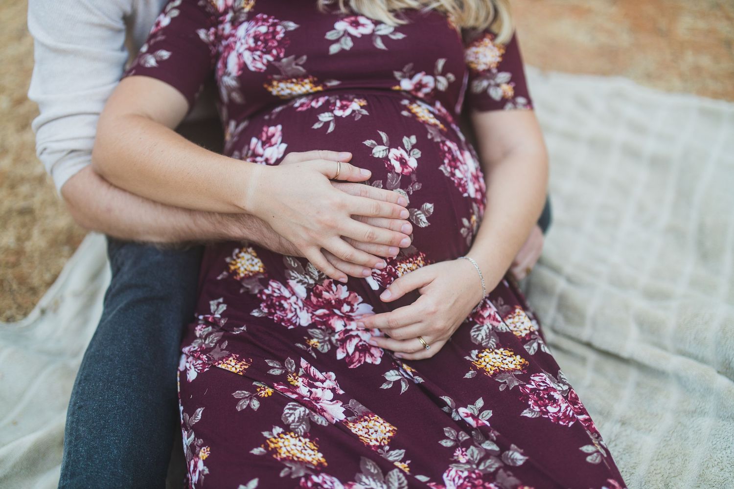 Close-up of hands resting on a burgundy floral dress showing an intimate moment.