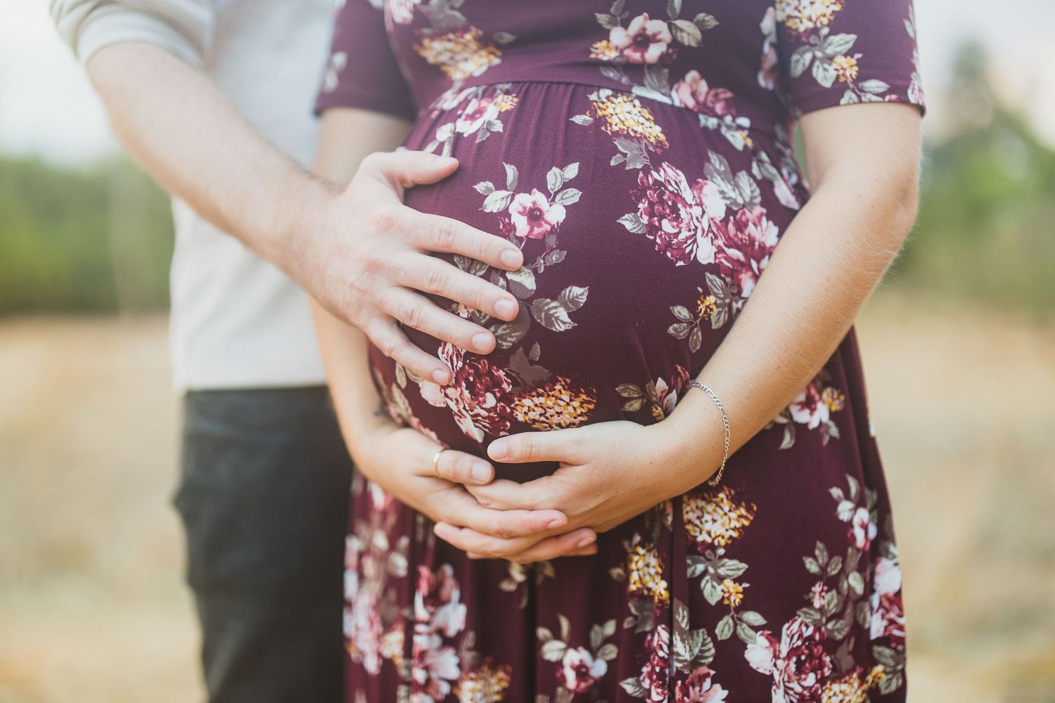 Close-up of hands cradling a pregnant belly in a purple floral maternity dress.
