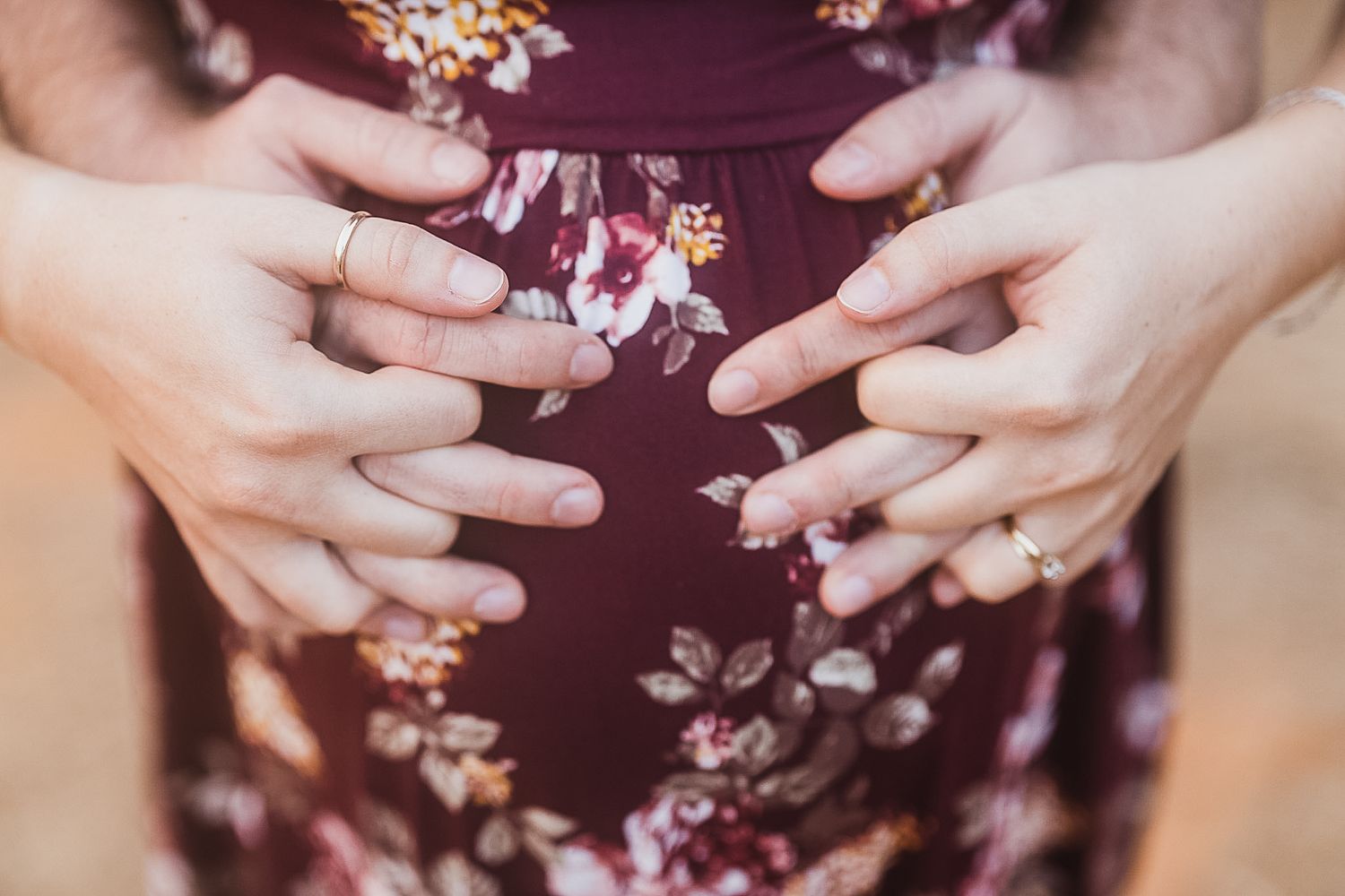 Close-up of hands framing a pregnant belly in burgundy floral dress.