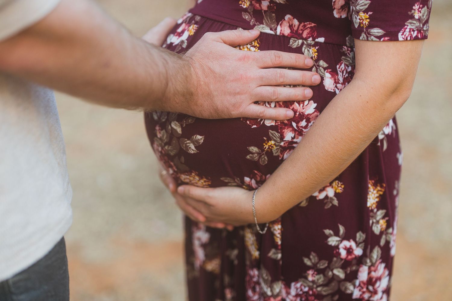 Hands tenderly resting on a pregnant belly covered in a burgundy floral dress.