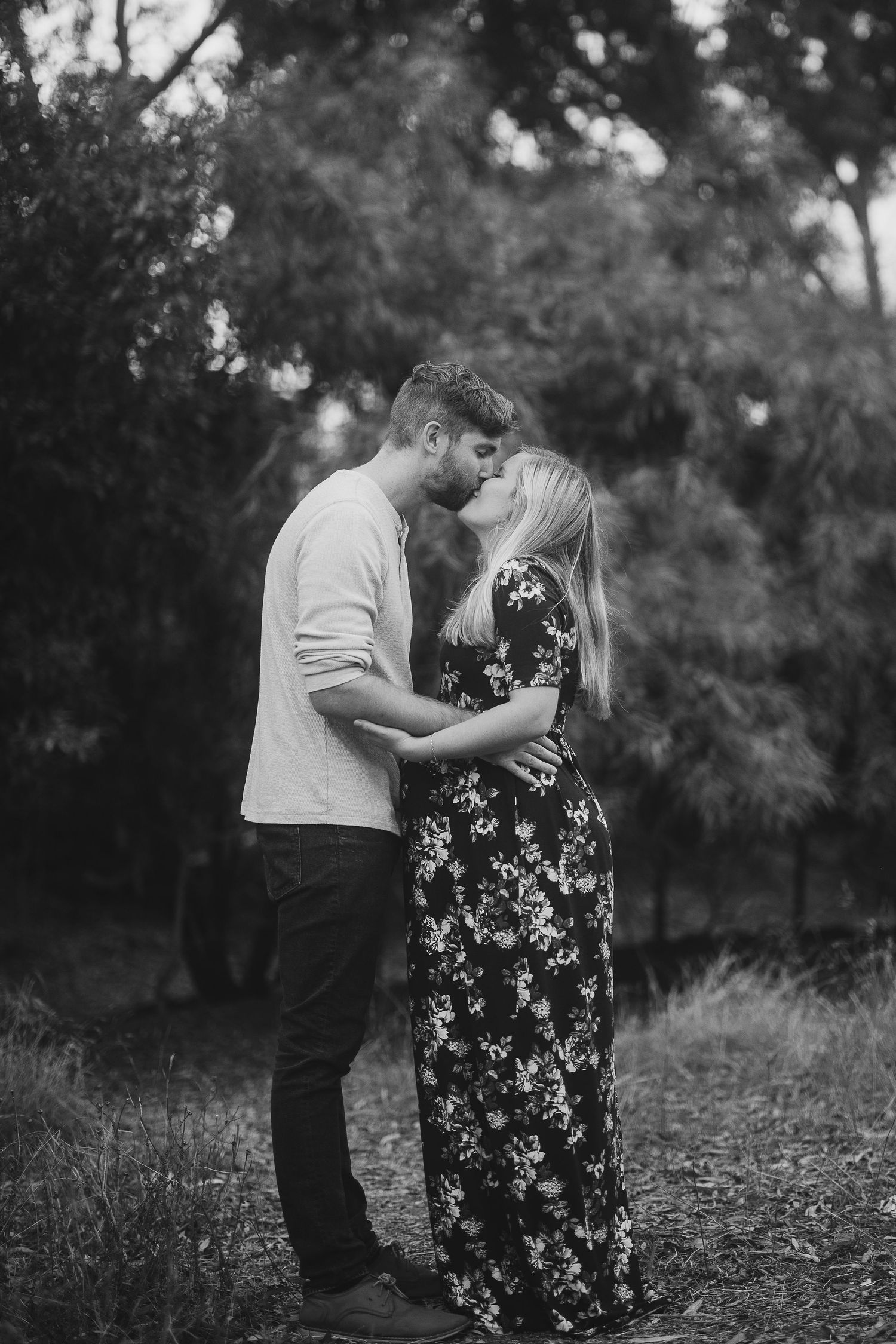 A romantic black and white portrait of a couple embracing outdoors.