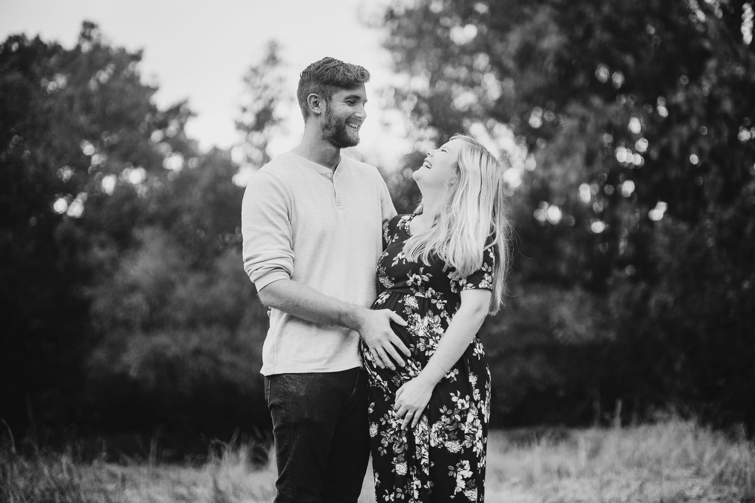 Romantic couple embracing in a black and white photo with trees in the background.