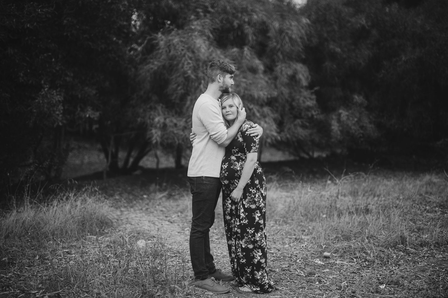 Black and white photo of a couple sharing a romantic moment in a wooded setting.