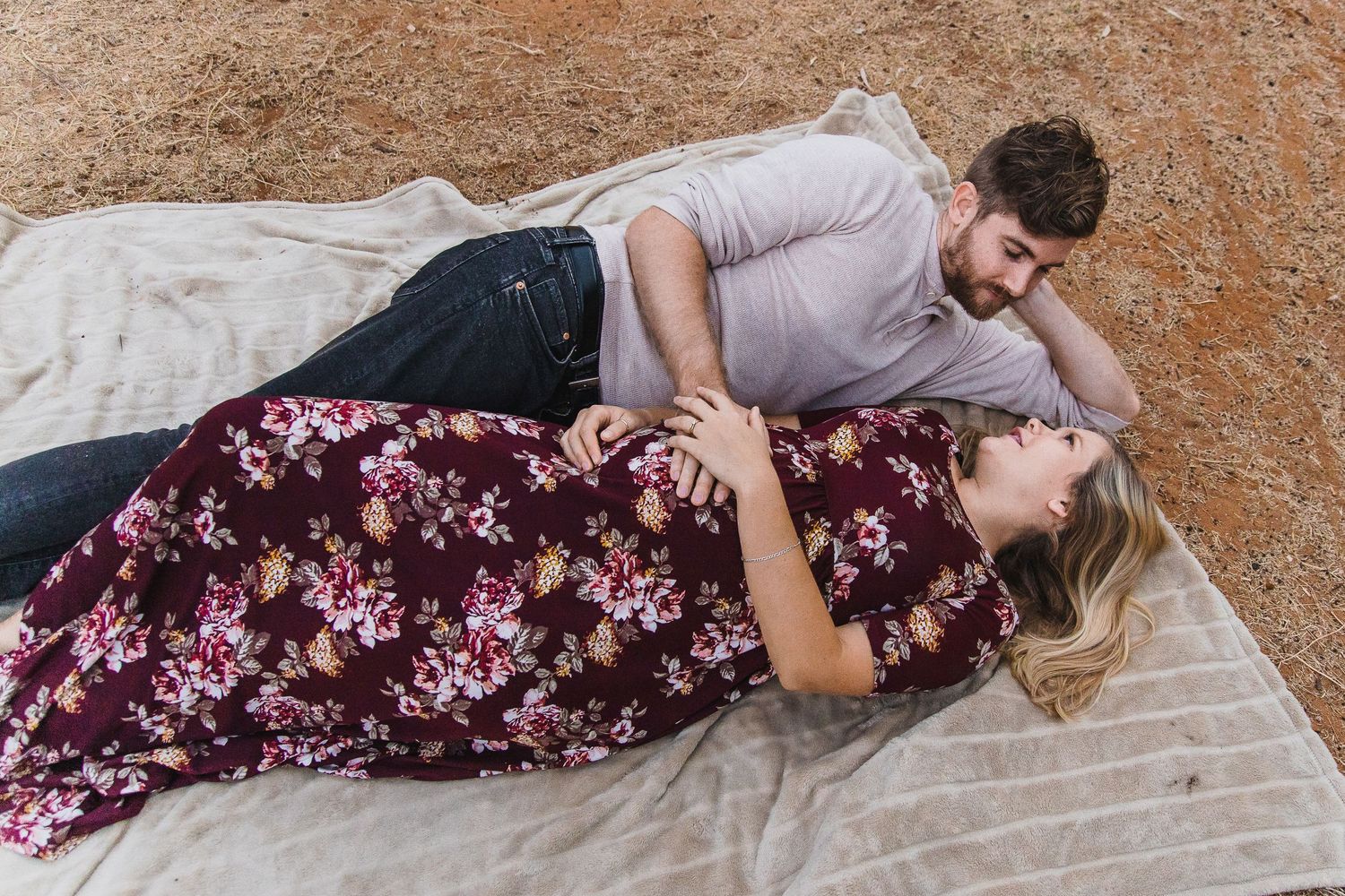 Two people in casual attire sharing playful moments on a white blanket outdoors.