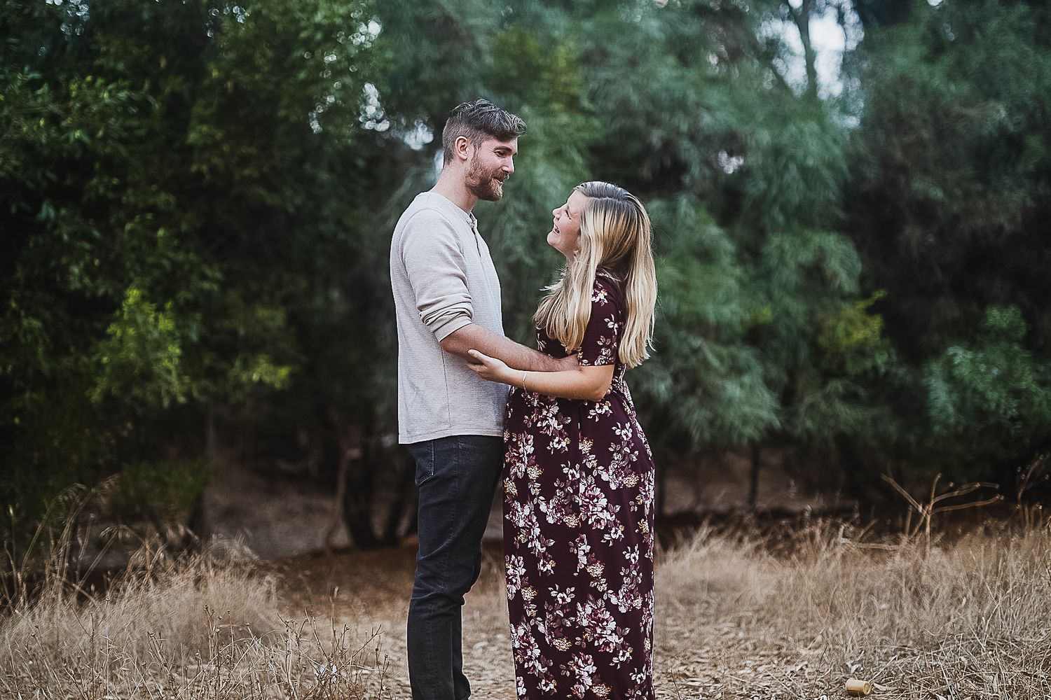Couple sharing tender moment in outdoor setting with natural backdrop.