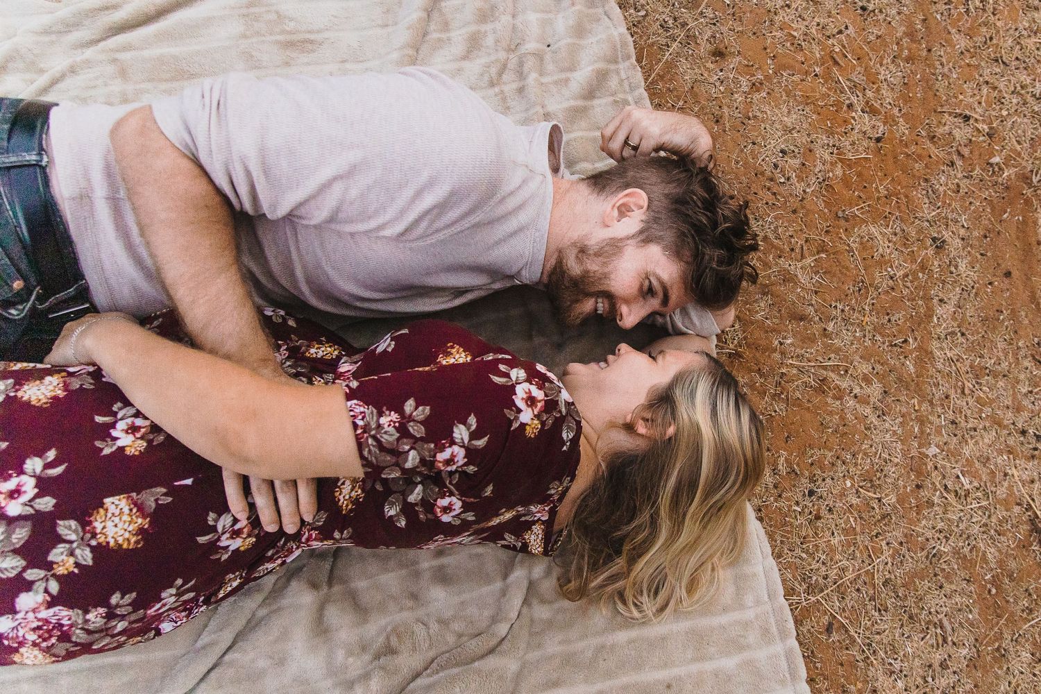 A couple sharing an intimate moment while lying on a blanket against a rustic backdrop.