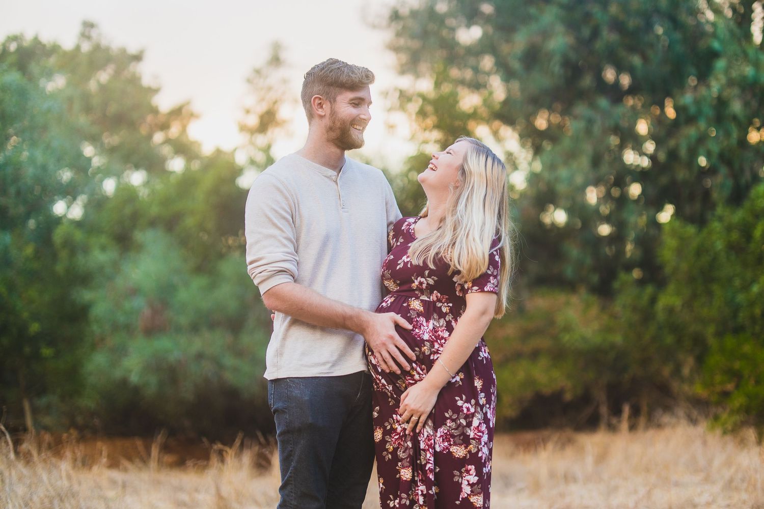 Couple shares an intimate moment at sunset in a field with trees.