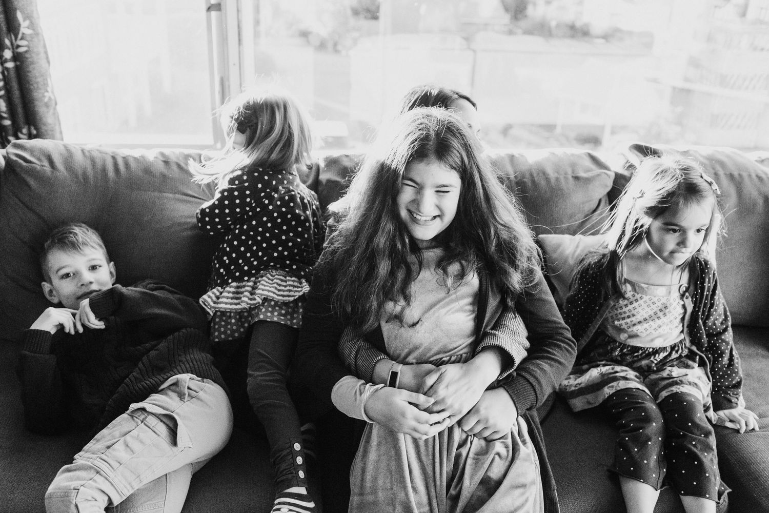 seattle lifestyle family photographer: four kids sitting on a couch. the eldest kid is on her mom's lap at an indoor photo session