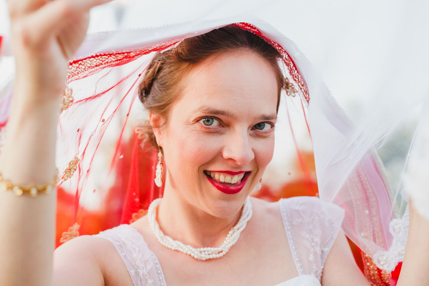A delicate red veil frames elegant bridal jewelry and makeup.