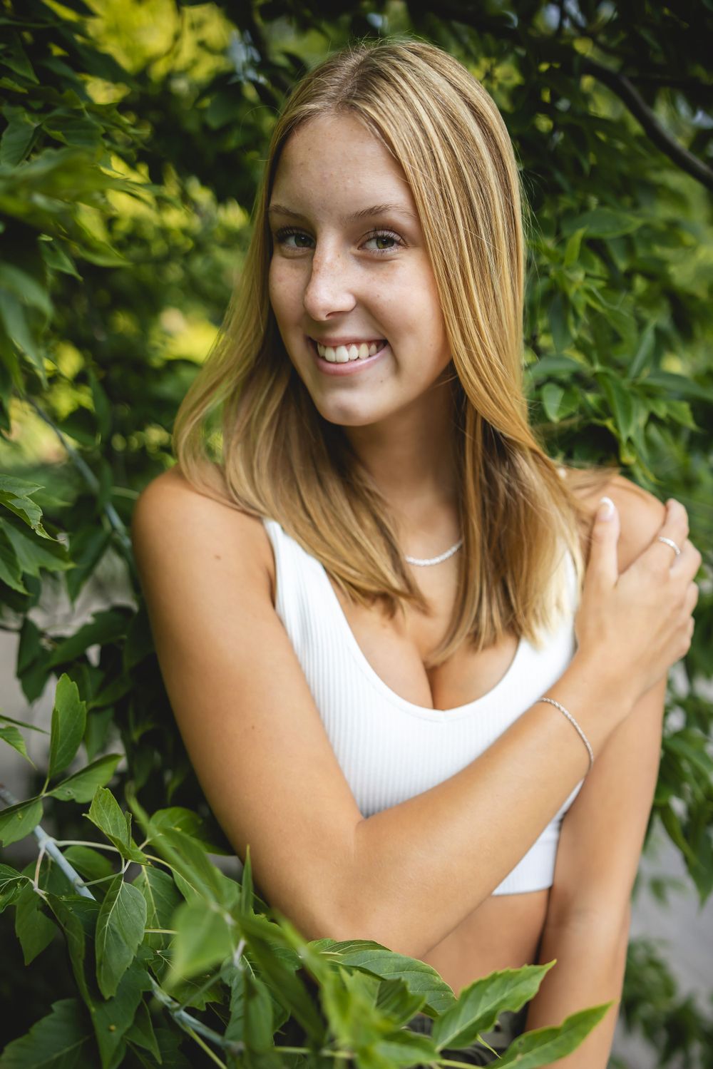 Summer portrait of someone smiling among green leaves wearing white.