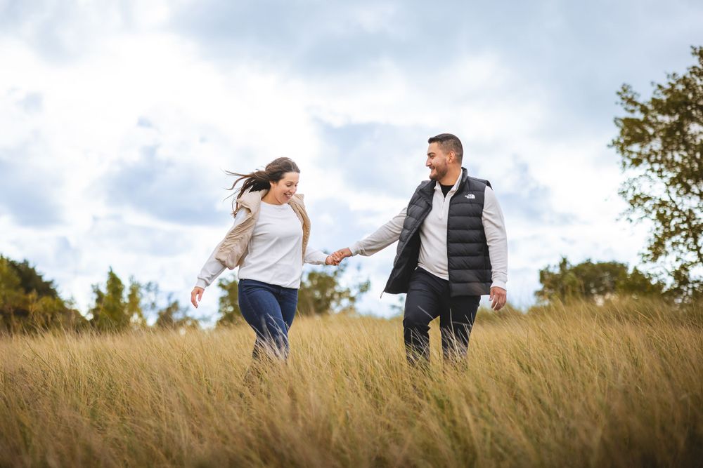 A couple running together through tall grass in a sunny field.