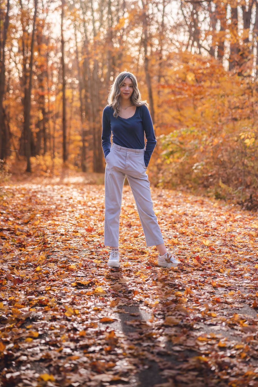 Full length fashion photo on a leaf-covered autumn path with warm orange tones.